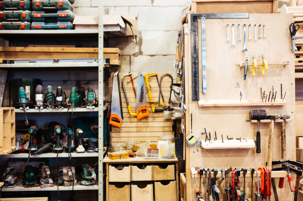 Organized workshop with saws, drills, wrenches, and measuring tools hanging on a wooden wall and shelves.