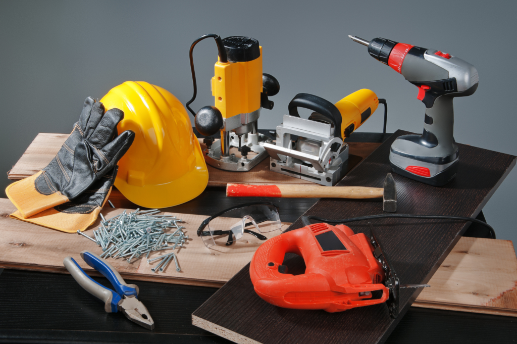 Assortment of construction tools including a yellow hard hat, power drill, jigsaw, screws, and safety